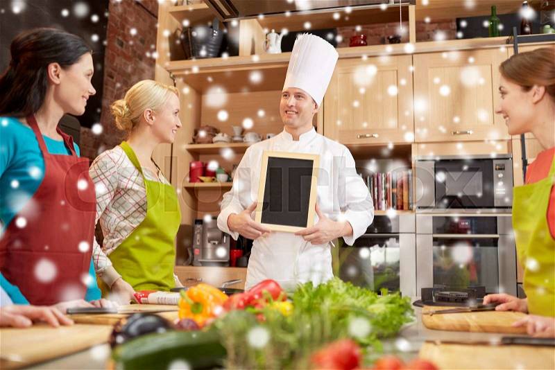 Cooking class, culinary, food and people concept - happy women and chef cook with blank menu chalk board in kitchen over snow effect, stock photo