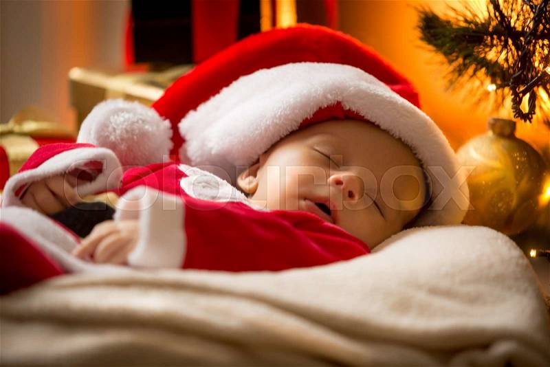Closeup portrait of sleeping baby boy in Santa cap at living room, stock photo