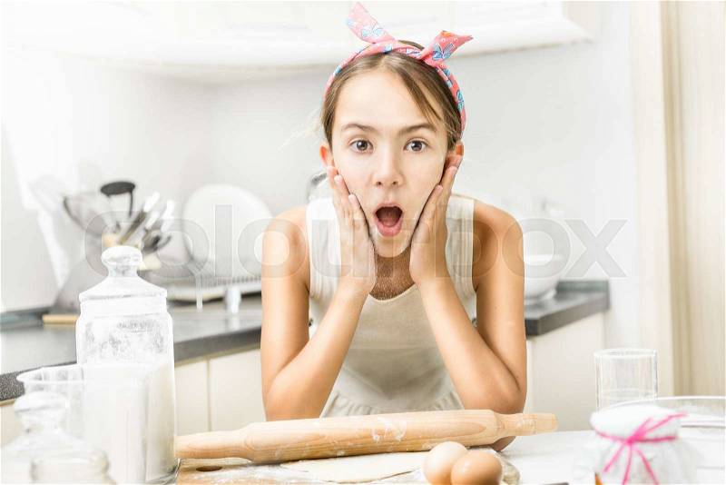 Portrait of excited girl clapping on her cheeks with flour while cooking, stock photo
