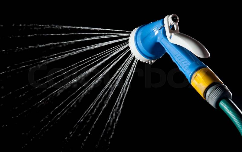 Hose nozzle spraying water on dark background, stock photo