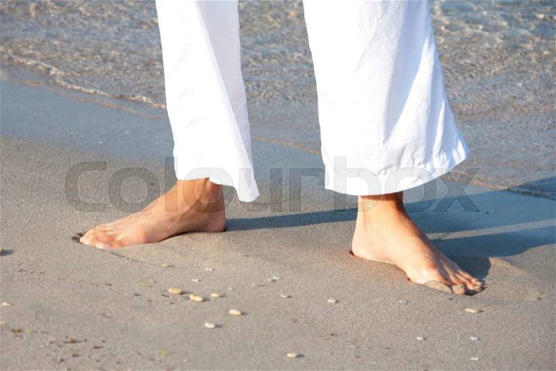 Woman in white walking barefoot on the beach, stock photo