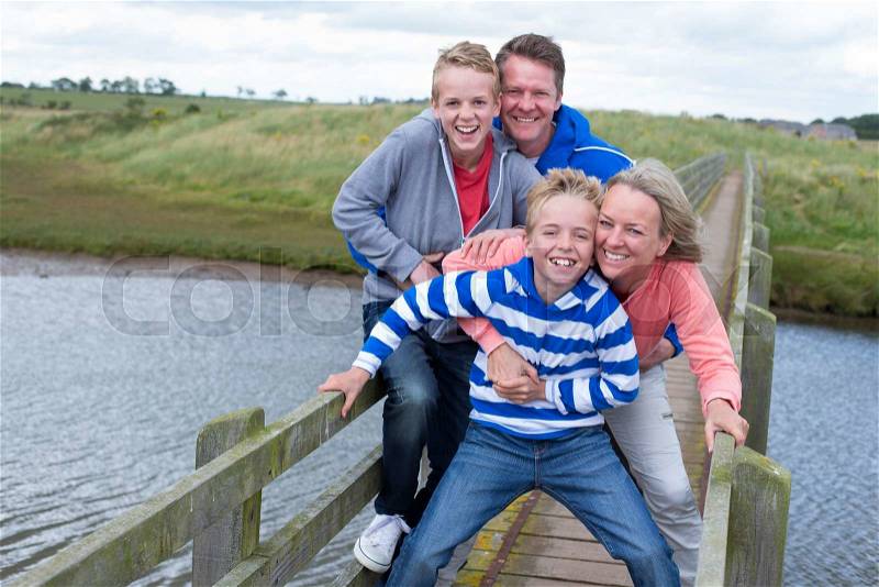 Family of four on a bridge over water. They are wearing casual clothing and smiling at the camera. , stock photo