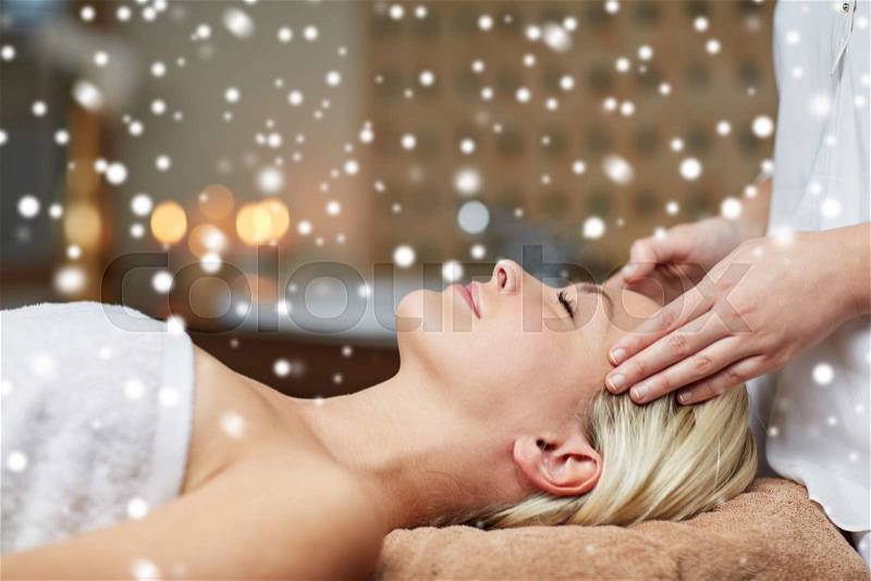 People, beauty, spa, winter and relaxation concept - close up of beautiful young woman lying with closed eyes and having face or head massage in spa with snow effect, stock photo