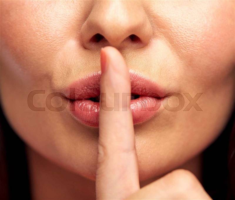 Silence, gesture and beauty concept - close up of young woman holding finger on lips, stock photo