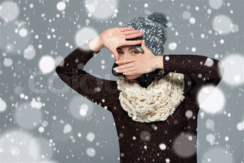 Pretty young woman in winter clothing making a frame with her hands, over snow background, stock photo