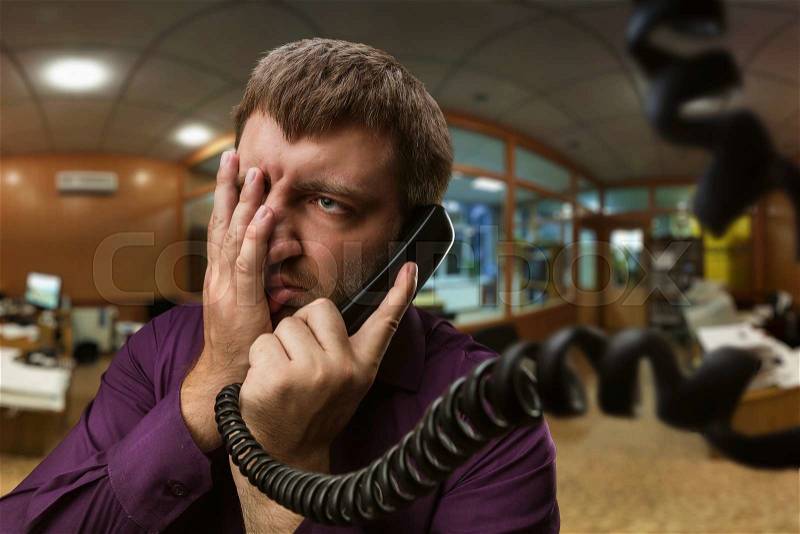 Frustrated bearded man speaks on the phone in the office, stock photo