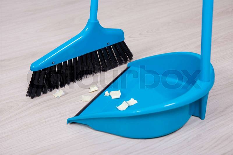 Close up of broom and dustpan with paper trash on wooden floor, stock photo