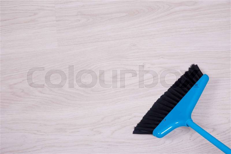 Cleaning concept - close up of blue broom sweeping wooden floor, stock photo