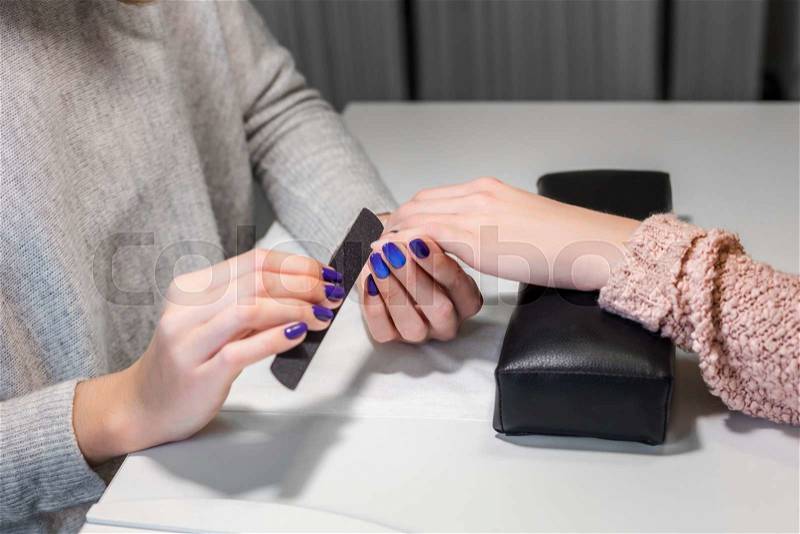 Processing nails with emery nail-file in beauty nail salon.Client receiving manicure by beautician. Gentle care of nails in cosmetic salon. Nail file. Manicure process, stock photo