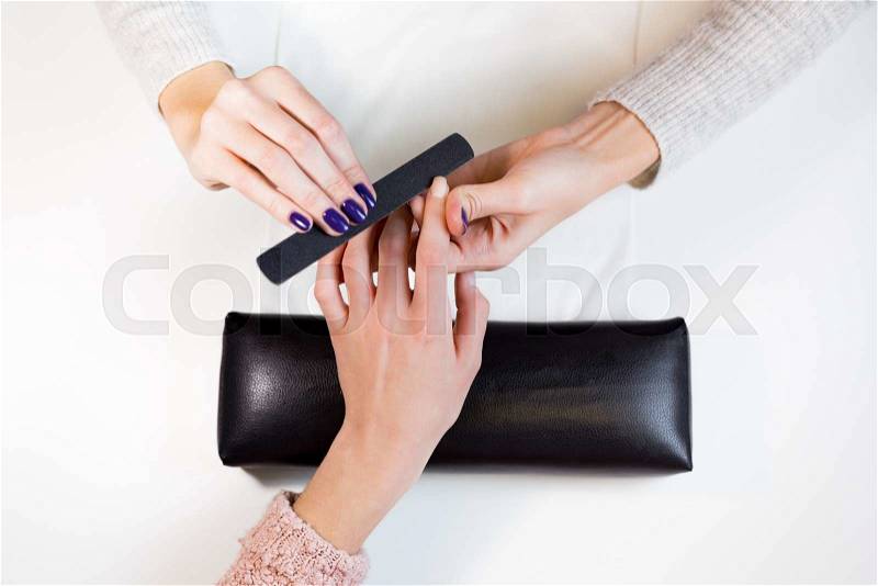 Top view manicurist polishing index finger for manicure in nail beauty salon. Step of manicure process, stock photo