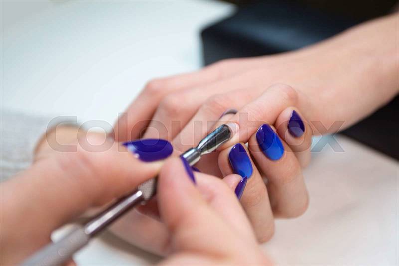Woman in nail salon receiving manicure by beautician.Manicurist removing cuticle from the nail of girl client at salon, stock photo