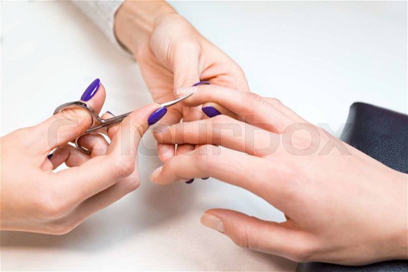 Top view closeup beautician works with nail scissors client ring finger on pure white table with professional tools for manicure and pedicure, stock photo