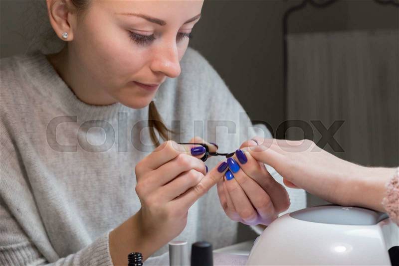 Nail polish being applied to hand, shellac is black color. Beautiful woman manicurist paintable lacquer on clients small finger in the spa salon, stock photo