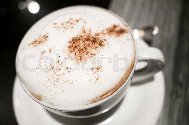 Cappuccino, cup of coffee with milk foam and cinnamon stands on black table in cafeteria, close up photo with selective focus, stock photo