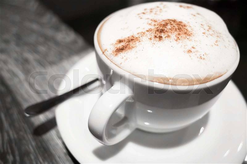 Cappuccino, cup of coffee with milk foam and cinnamon stands on black table in cafeteria, close-up photo with selective focus, stock photo