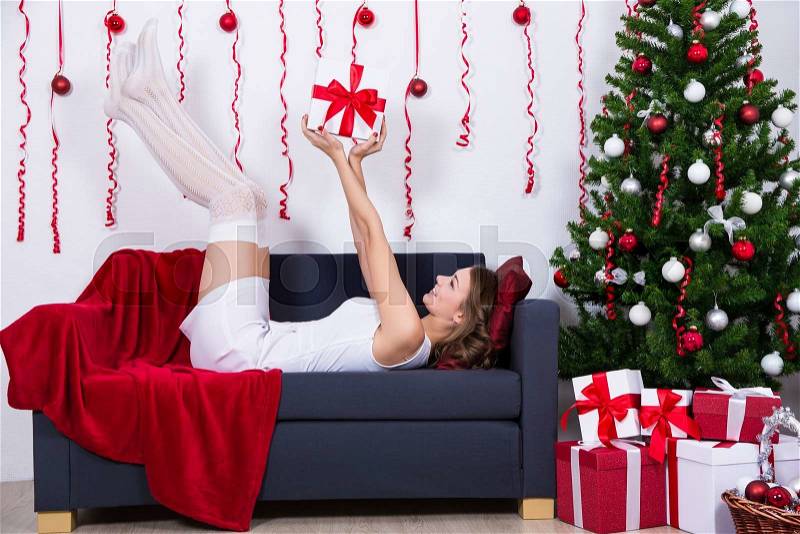 Happy young beautiful woman lying on sofa with decorated Christmas tree at home, stock photo
