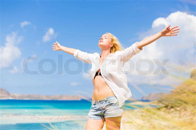 Relaxed woman enjoying freedom and life an a beautiful sandy beach. Young lady raising arms, feeling free, relaxed and happy. Concept of freedom, happiness, enjoyment and well being, stock photo