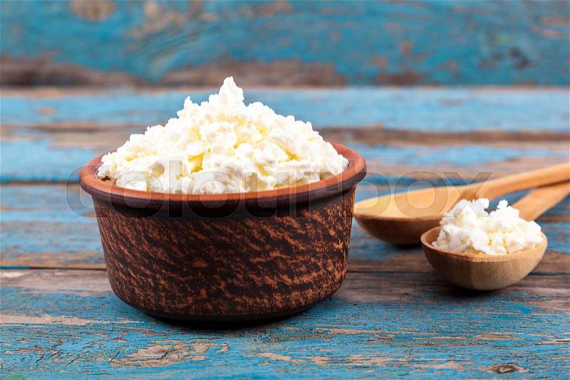 Fresh cottage cheese in a ceramic dish and spoon on painted blue wooden boards, stock photo