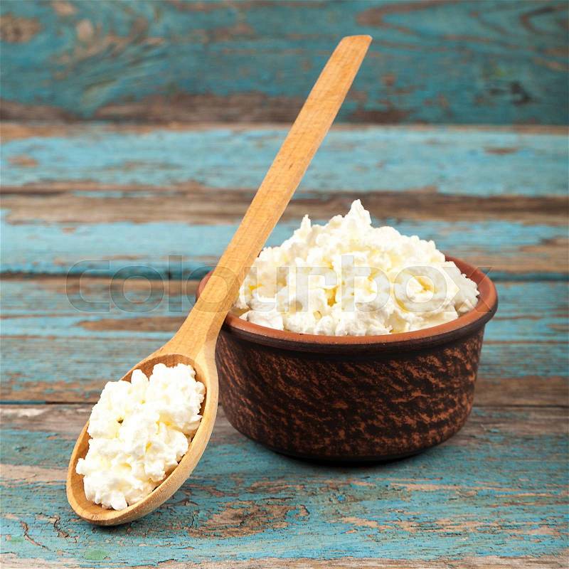 Fresh cottage cheese in a ceramic dish and spoon on painted blue wooden boards, stock photo