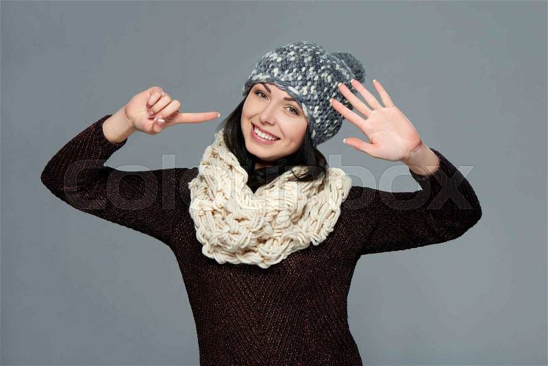 Hand counting - six fingers. Portrait of woman on grey background wearing woolen hat and muffler showing six fingers, stock photo