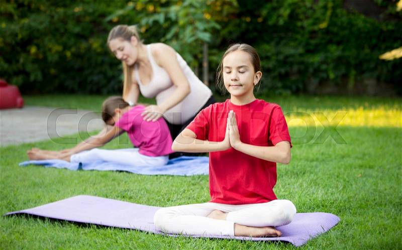 Portrait of cute girl doing yoga during outdoor lesson at park, stock photo