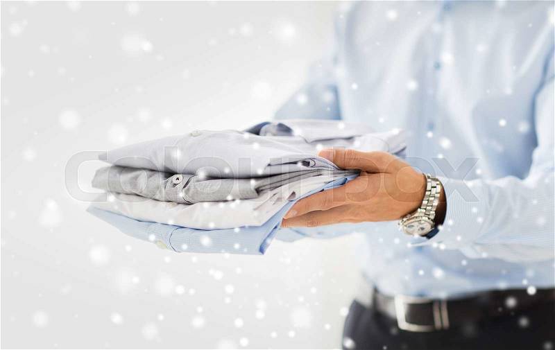 Business, clothing and people concept - close up of businessman holding folded shirts over snow effect, stock photo