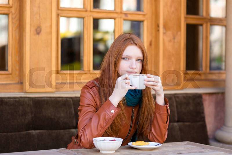Pensive woman sitting with coffee cup and has a rest in spring cafe outdoors and dreaming looking far away, stock photo