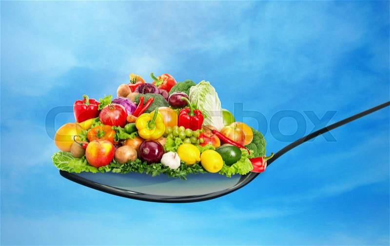 Spoon full of various fruit and vegetables on blue sky, stock photo