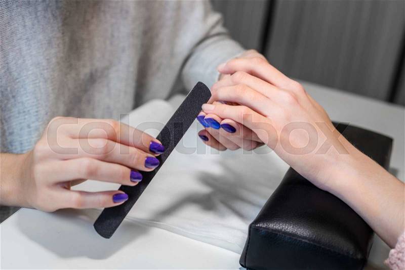 Closeup picture of manicure process on female hands in beauty nail salon. Manicurist nail file works, stock photo