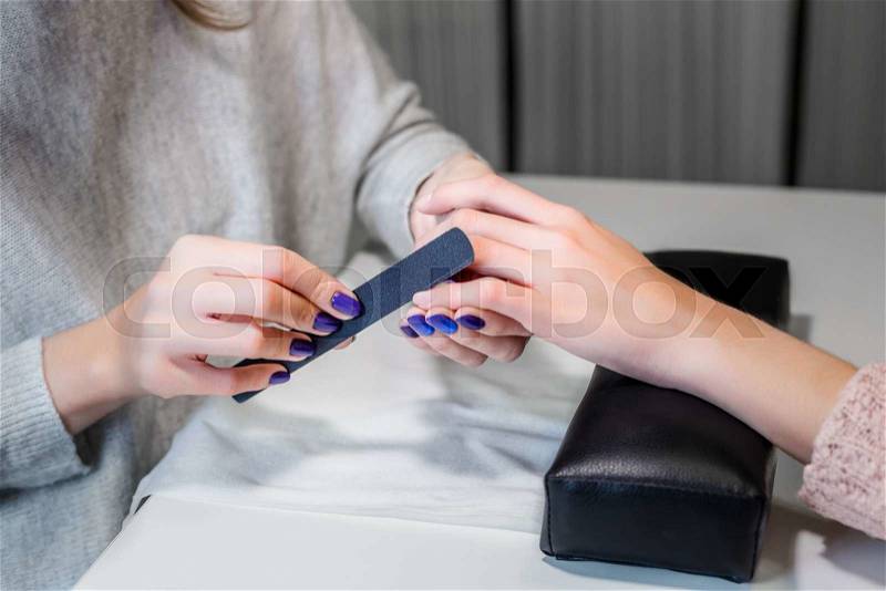 Closeup picture of manicure master nail file works in salon. On white table laid out beauty tools. , stock photo