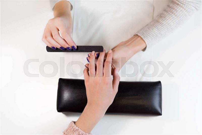 Top view manicurist nail file works on the ring finger. Closeup image of hands polishing fingers on towel in beauty salon, stock photo