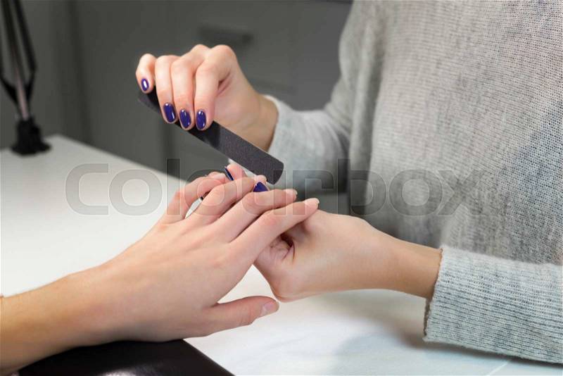Professional process of manicure by nail file in white beauty salon.Manicurist gently manicured service. Hand on the black professional pillow, stock photo