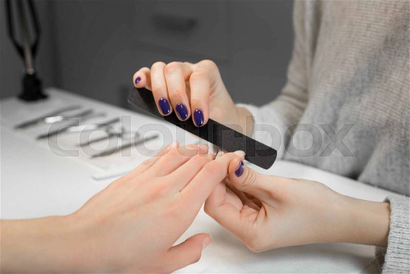 Manicure process with nail file in beauty salon. Manicure makes service beautiful girl client.On background are instruments manicure and pedicure, stock photo