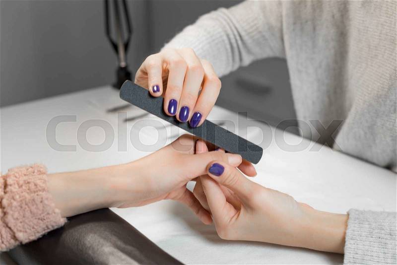 Beautician filing female clients thumb and nails at spa beauty salon.Manicurist work on pure white table with professional tools for manicure and pedicure, stock photo