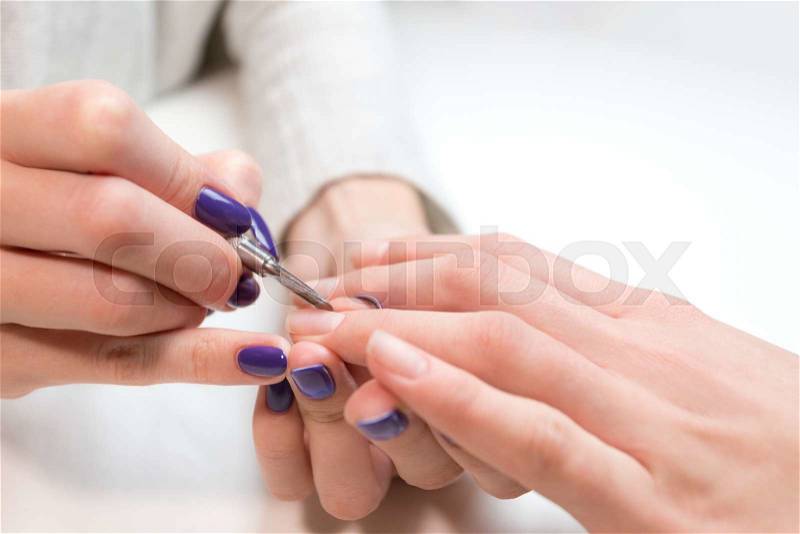 Manicurist removing cuticle from ring finger of girl client at beauty salon. Manicurist work on pure white table with professional tools for manicure and pedicure, stock photo