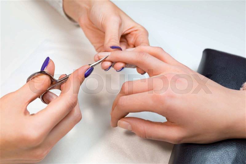 Closeup manicurist cut clients cuticle with nail scissors in salon nail salon or spa. Hand lies on a glass white napkin, stock photo