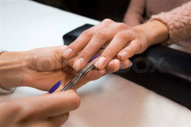 Closeup of picture removing the cuticle by manicure nippers in beauty nail salon. Manicurist work professional tools on clean white table, stock photo