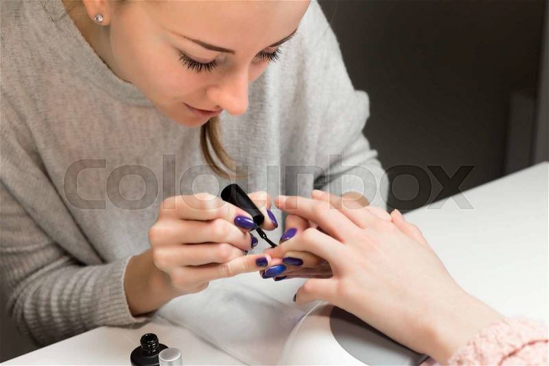 Process of doing manicure in the spa salon. Beautician applying black nail polish on the nails in the beauty salon. The concept of hand care, stock photo