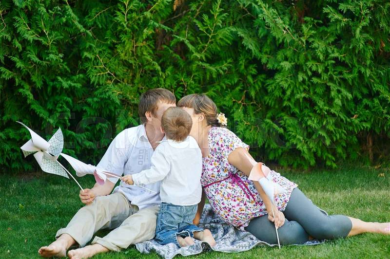 Dad mom and son sitting on a blanket in the park and kiss, stock photo