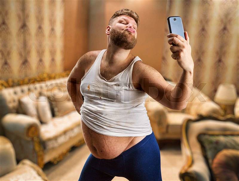 Fat glamour man with beard takes selfie in his bedroom, stock photo