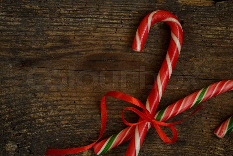 Closeup of two old fashioned candy canes on a rustic wooden background. The treats are crossed and tied with a red ribbon, stock photo