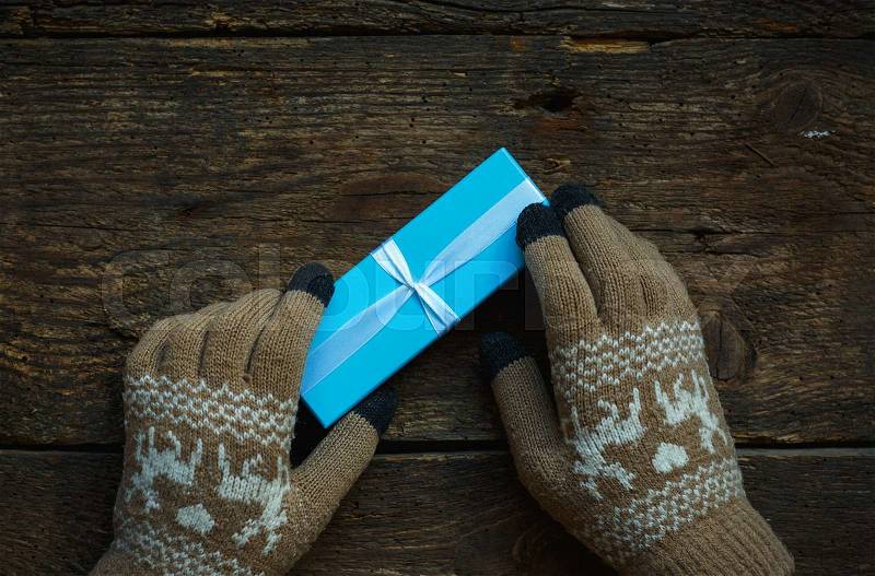 Female hands in winter gloves with christmas gift box on wooden background, stock photo