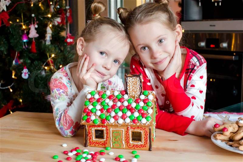Little adorable girls decorating gingerbread house for Christmas at home, stock photo