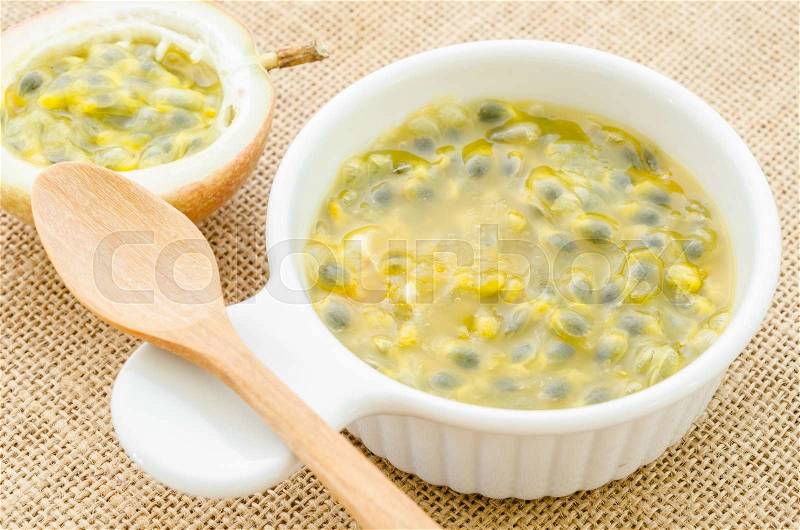 Passion fruit juice in white cup with wooden spoon on sack background, stock photo