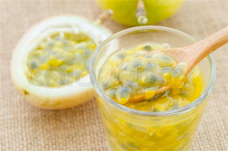 Passion fruit juice in glass with wooden spoon on sack background, stock photo