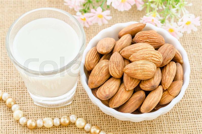 Almond milk in glass and almonds in white cup with flower on sack background, stock photo