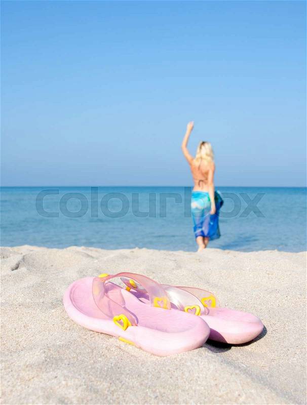 Flip flops on the beach with going for a swim woman on background, stock photo