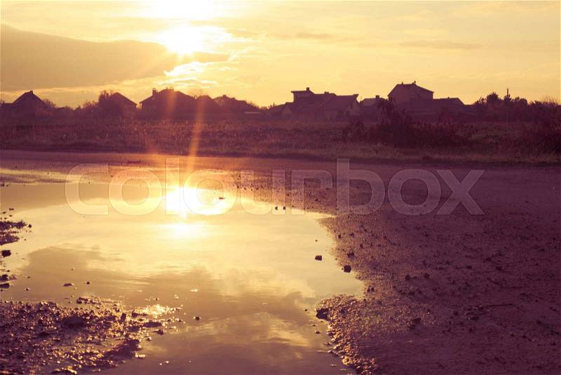 The sunset reflected in a deep puddle on a dirt road, stock photo