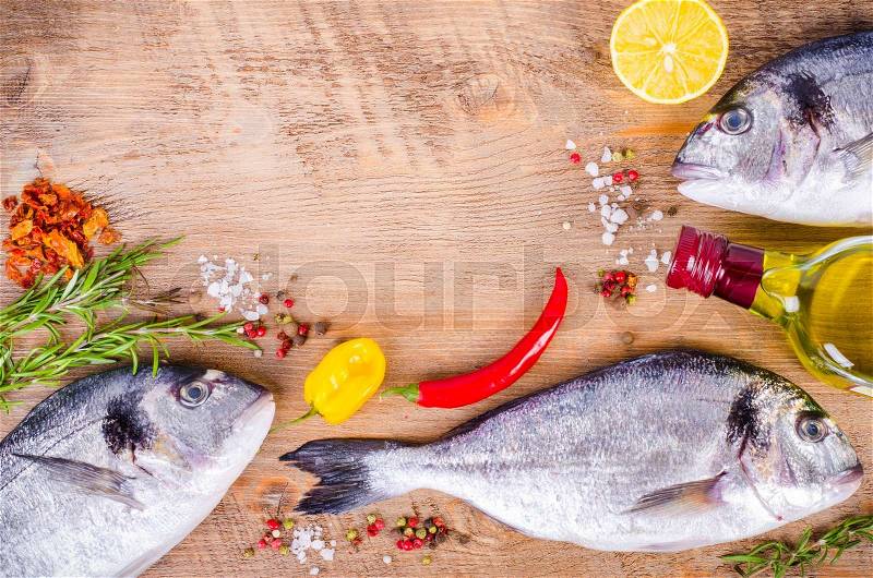 Fresh raw gilthead fishes with lemon, herbs, olive oil, salt on wooden background. Healthy food concept. Food frame, stock photo