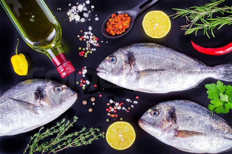 Fresh raw gilthead fishes with lemon, herbs, salt on black background. Healthy food concept. Food frame, stock photo